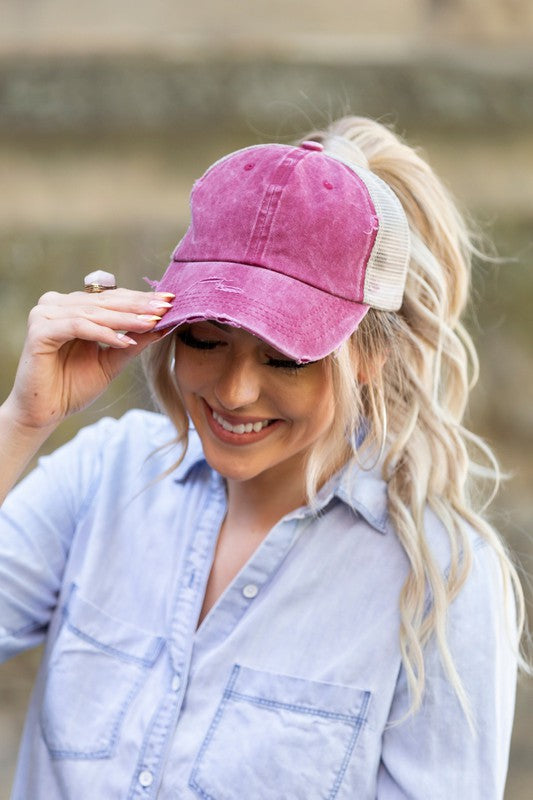 Woman smiling and tipping her gray, Distressed Messy Bun Hat Cap.