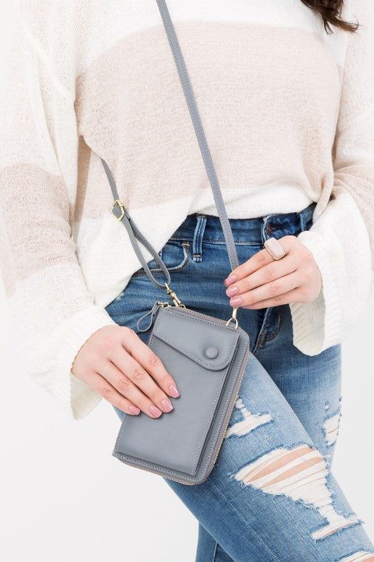 A person dressed in a gray sweater and ripped jeans carries their phone in a stylish pink Cross Body Convertible Wallet made of vegan leather, displaying purple nail polish.