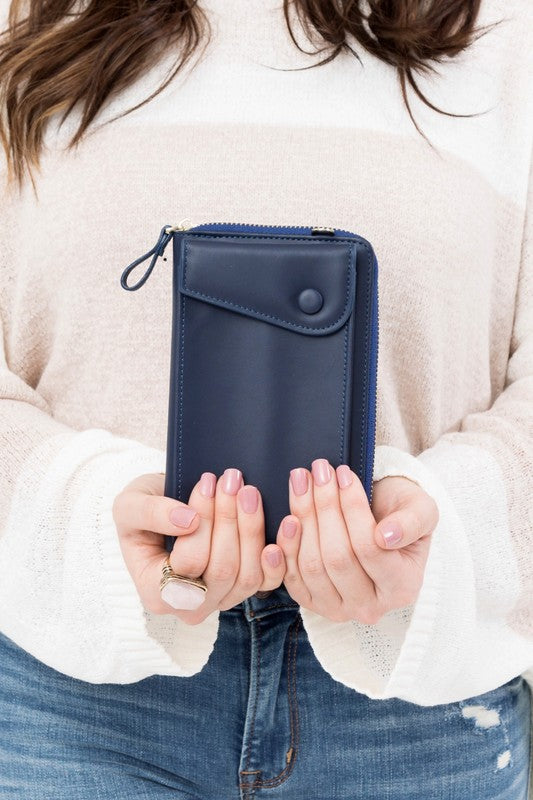 A person dressed in a gray sweater and ripped jeans carries their phone in a stylish pink Cross Body Convertible Wallet made of vegan leather, displaying purple nail polish.