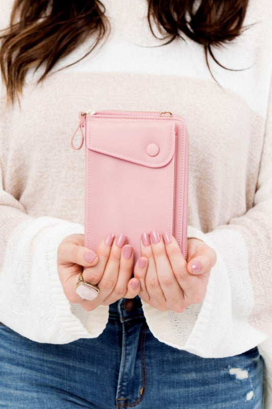 A person dressed in a gray sweater and ripped jeans carries their phone in a stylish pink Cross Body Convertible Wallet made of vegan leather, displaying purple nail polish.