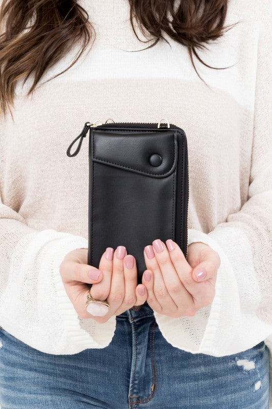 A person dressed in a gray sweater and ripped jeans carries their phone in a stylish pink Cross Body Convertible Wallet made of vegan leather, displaying purple nail polish.