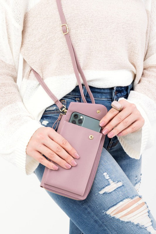 A person dressed in a gray sweater and ripped jeans carries their phone in a stylish pink Cross Body Convertible Wallet made of vegan leather, displaying purple nail polish.