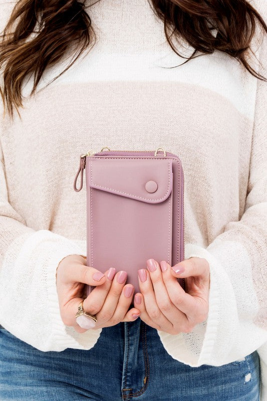 A person dressed in a gray sweater and ripped jeans carries their phone in a stylish pink Cross Body Convertible Wallet made of vegan leather, displaying purple nail polish.