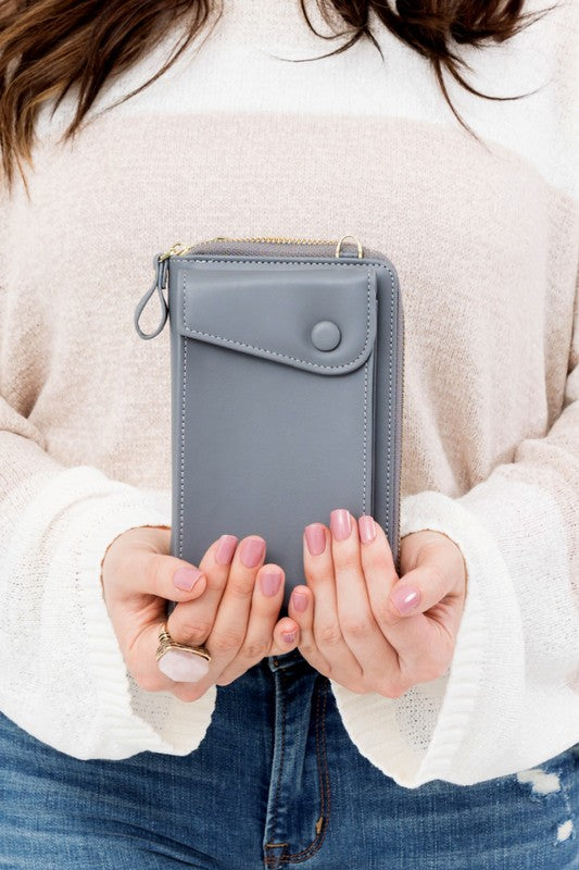 A person dressed in a gray sweater and ripped jeans carries their phone in a stylish pink Cross Body Convertible Wallet made of vegan leather, displaying purple nail polish.