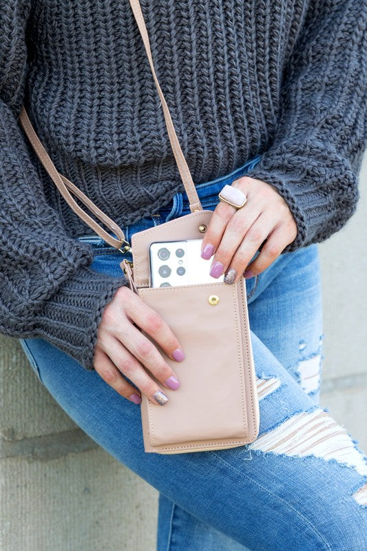 A person dressed in a gray sweater and ripped jeans carries their phone in a stylish pink Cross Body Convertible Wallet made of vegan leather, displaying purple nail polish.