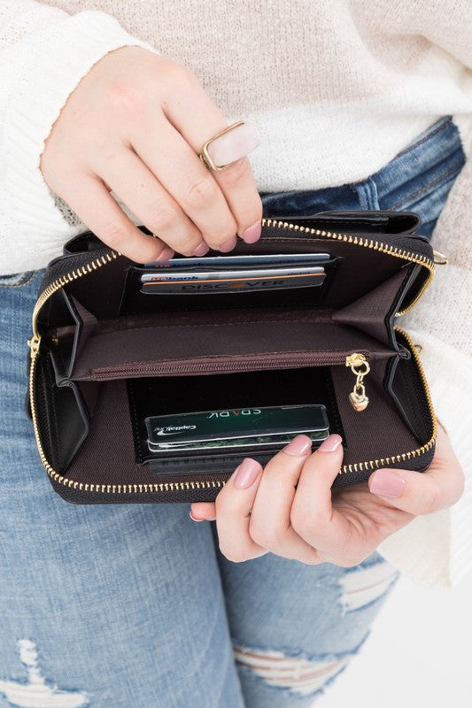 A person dressed in a gray sweater and ripped jeans carries their phone in a stylish pink Cross Body Convertible Wallet made of vegan leather, displaying purple nail polish.