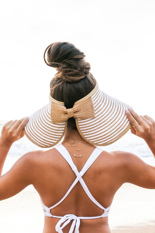 A woman from behind wearing a white bikini and a wide-brimmed, breathable Foldable Bow Stripe Visor on the beach.