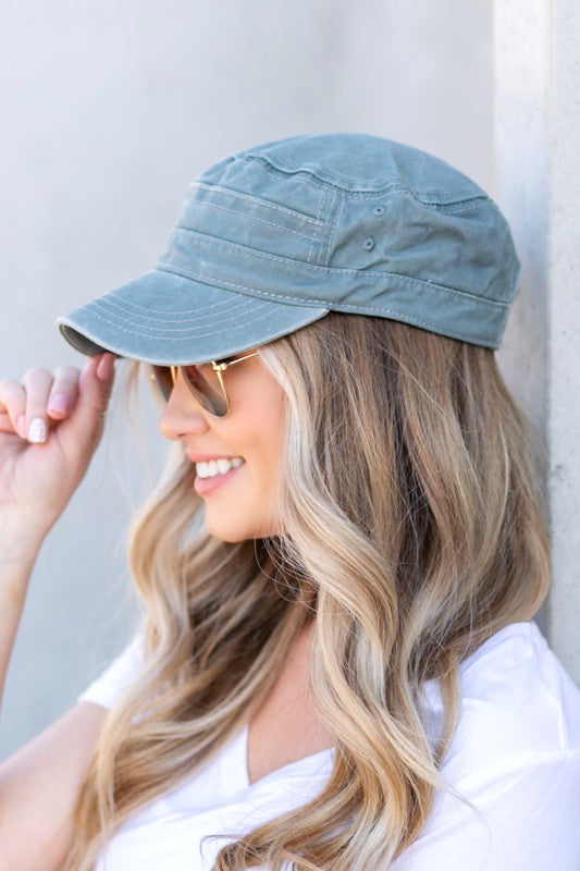 Woman in a white t-shirt and military-inspired black Distressed Cadet Hat Cap with an adjustable clasp, smiling at the camera.