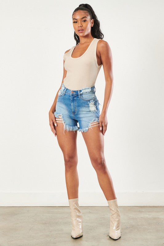 A person poses in a beige tank top, distressed vintage wash Denim Short, and beige ankle boots against a plain white background, perfectly capturing the casual and trendy vibe.