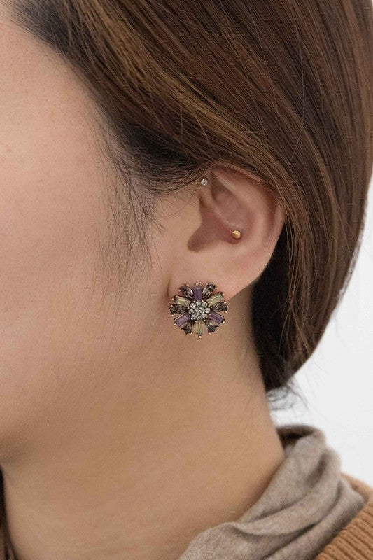 The Liesel Stud Earrings feature a floral design with vibrant purple and gray stones on a light background.