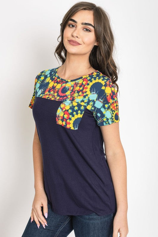 A woman smiles with her hands clasped, dressed in the Medallion Front Pocket Tunic, featuring a dark blue base with colorful, patterned sleeves.