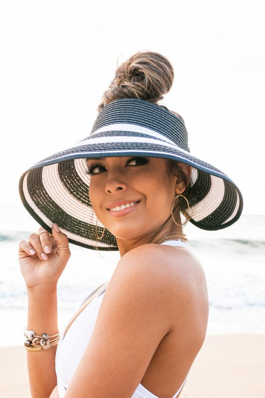 Woman holding her Foldable Wide Stripe Bow Visor on a beach, viewed from behind.