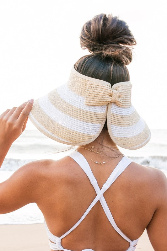 Woman holding her Foldable Wide Stripe Bow Visor on a beach, viewed from behind.