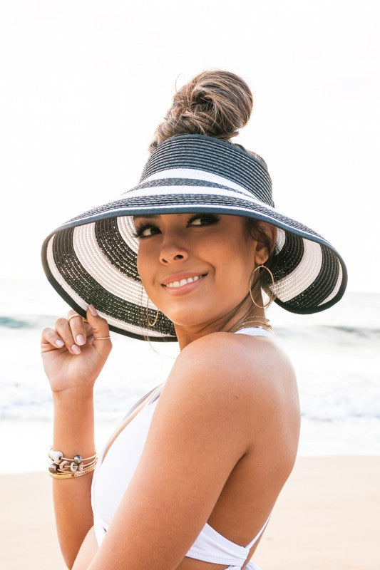 Woman holding her Foldable Wide Stripe Bow Visor on a beach, viewed from behind.