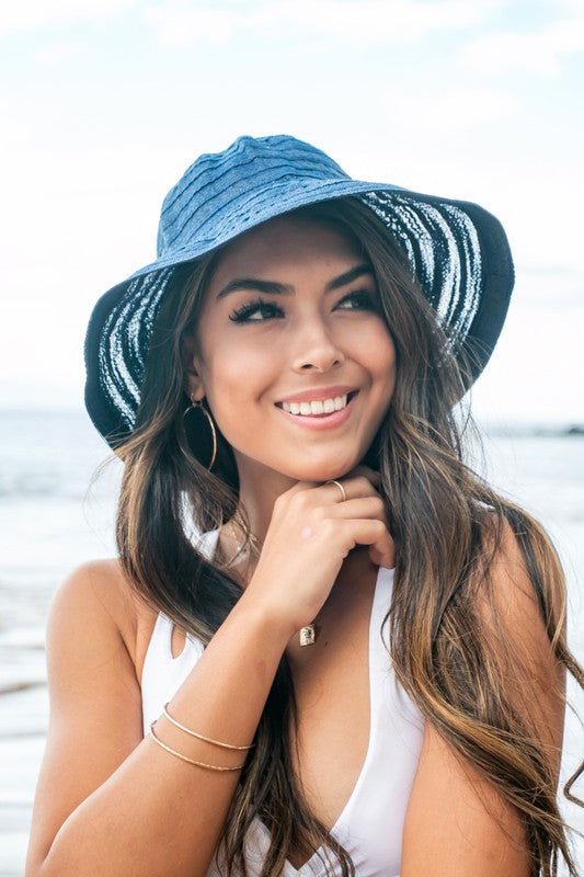 A smiling woman adjusting her Bow Accent Bucket Sunhat at the beach.
