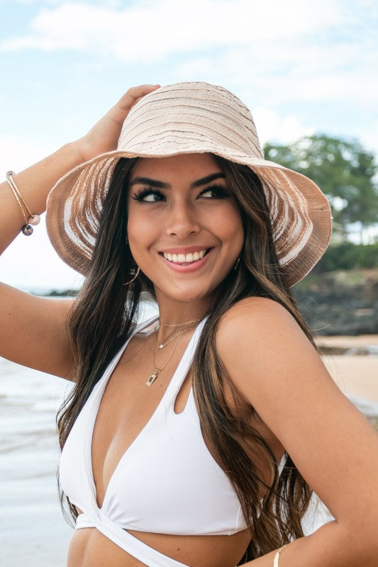 Woman smiling and holding her Bow Accent Bucket Sunhat on a beach.