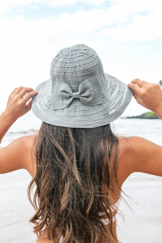 A smiling woman adjusting her Bow Accent Bucket Sunhat at the beach.