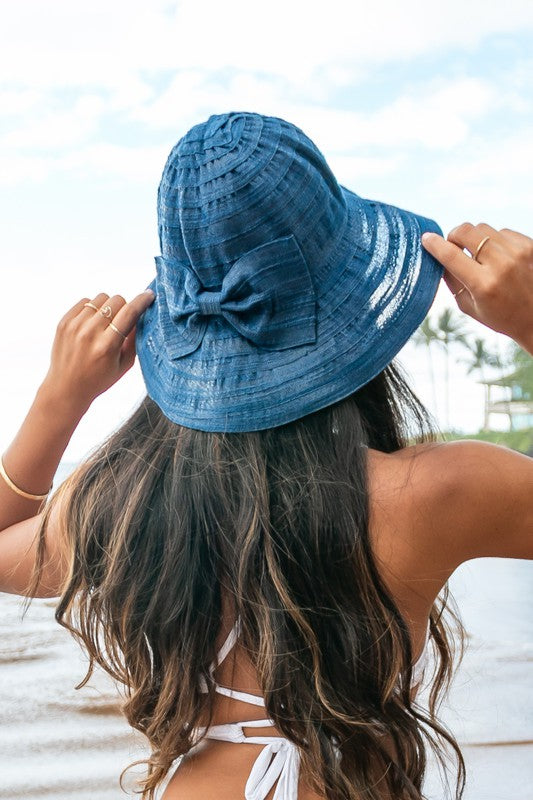 A smiling woman adjusting her Bow Accent Bucket Sunhat at the beach.
