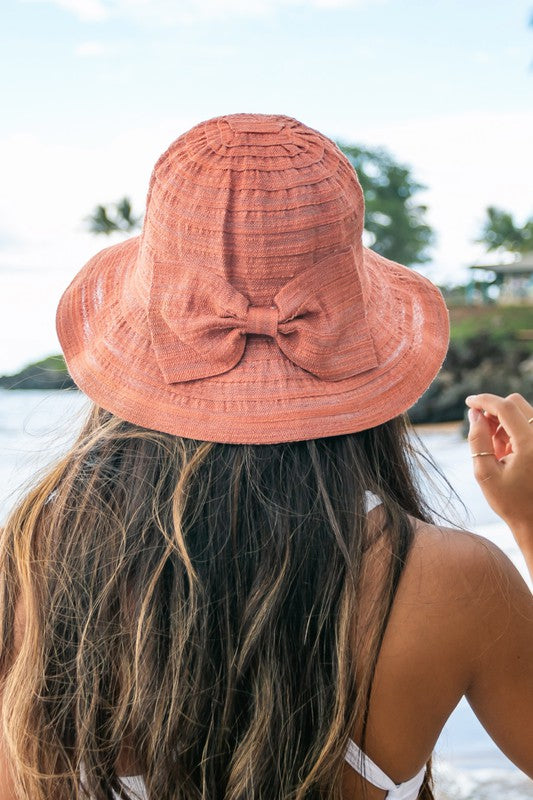 A smiling woman adjusting her Bow Accent Bucket Sunhat at the beach.