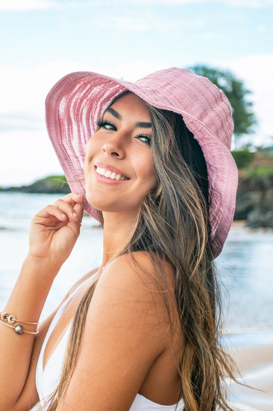 A smiling woman adjusting her Bow Accent Bucket Sunhat at the beach.