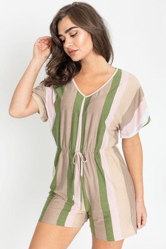 Dressed in the Summer Stripe Surplice Romper, featuring vertical stripes in green, beige, and pink, one highlights its handcrafted elegance. Made in the United States, it makes a striking impression against a plain white backdrop.