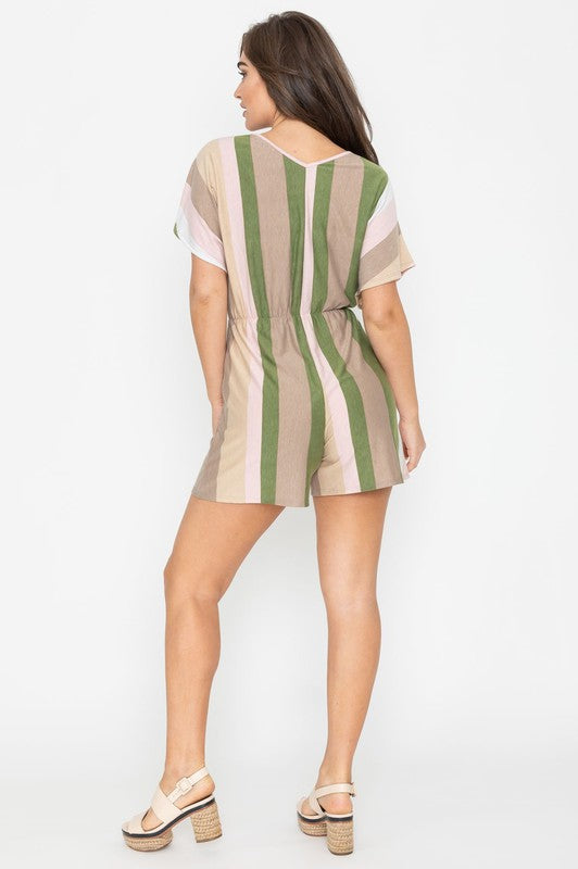 Dressed in the Summer Stripe Surplice Romper, featuring vertical stripes in green, beige, and pink, one highlights its handcrafted elegance. Made in the United States, it makes a striking impression against a plain white backdrop.