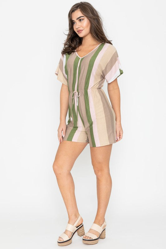 Dressed in the Summer Stripe Surplice Romper, featuring vertical stripes in green, beige, and pink, one highlights its handcrafted elegance. Made in the United States, it makes a striking impression against a plain white backdrop.