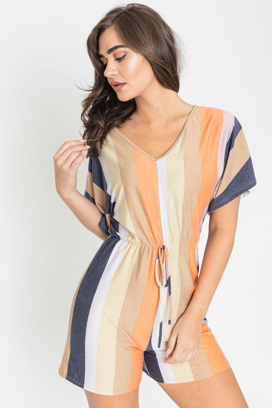 Dressed in the Summer Stripe Surplice Romper, featuring vertical stripes in green, beige, and pink, one highlights its handcrafted elegance. Made in the United States, it makes a striking impression against a plain white backdrop.