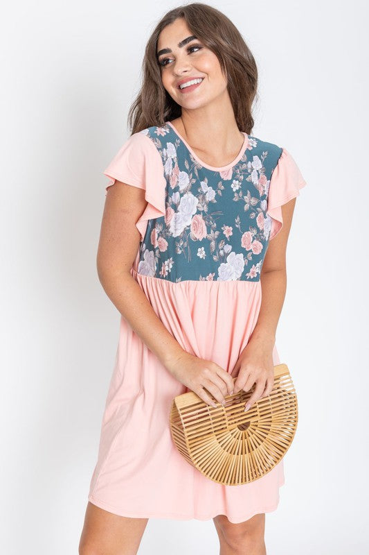 A woman wearing the Flutter Sleeve Rose Floral Mini Dress stands gracefully against a plain background, holding a wooden clutch bag.