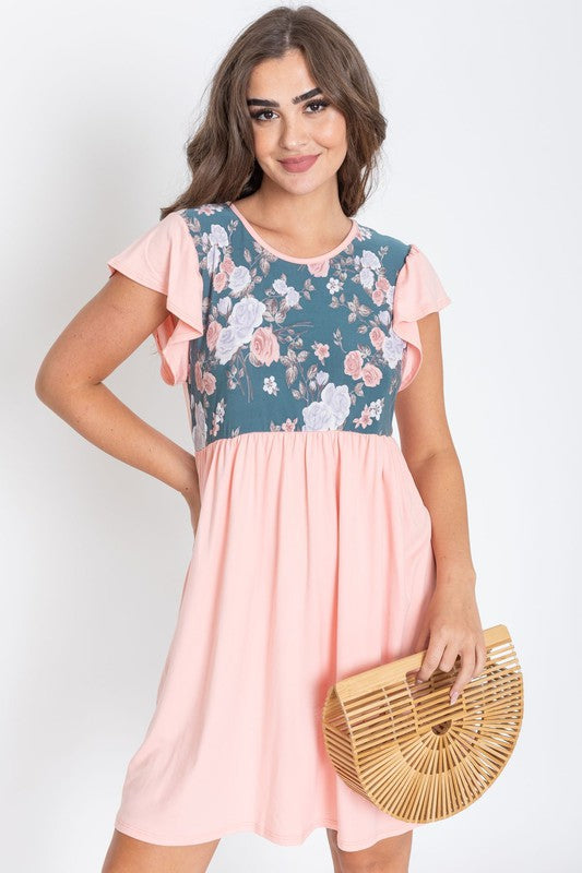 A woman wearing the Flutter Sleeve Rose Floral Mini Dress stands gracefully against a plain background, holding a wooden clutch bag.