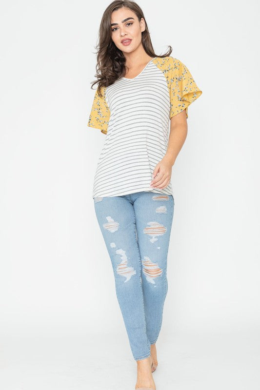 A woman is standing and smiling in a V Neck Stripe Floral Sleeve Tunic, paired perfectly with distressed jeans.