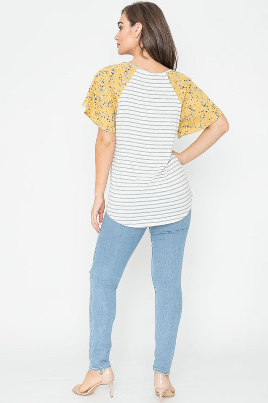 A woman is standing and smiling in a V Neck Stripe Floral Sleeve Tunic, paired perfectly with distressed jeans.