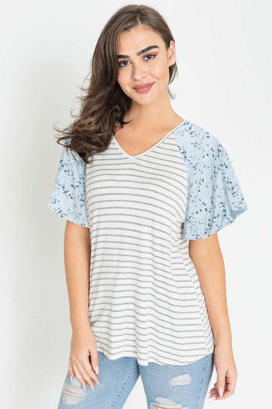 A woman is standing and smiling in a V Neck Stripe Floral Sleeve Tunic, paired perfectly with distressed jeans.