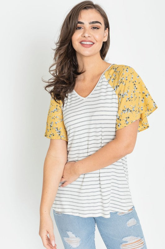 A woman is standing and smiling in a V Neck Stripe Floral Sleeve Tunic, paired perfectly with distressed jeans.