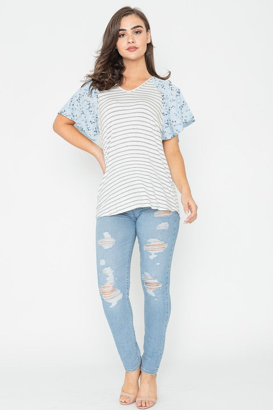 A woman is standing and smiling in a V Neck Stripe Floral Sleeve Tunic, paired perfectly with distressed jeans.