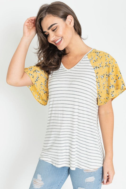 A woman is standing and smiling in a V Neck Stripe Floral Sleeve Tunic, paired perfectly with distressed jeans.