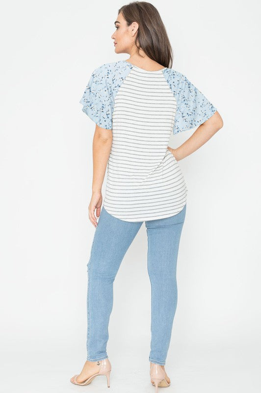 A woman is standing and smiling in a V Neck Stripe Floral Sleeve Tunic, paired perfectly with distressed jeans.