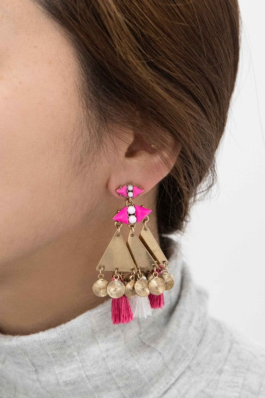 The Leinani Tassel Earrings feature gold triangles, pink and white tassels, and are adorned with small round charms in a bohemian style.