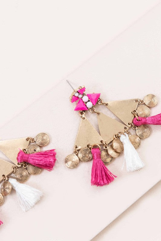 The Leinani Tassel Earrings feature gold triangles, pink and white tassels, and are adorned with small round charms in a bohemian style.