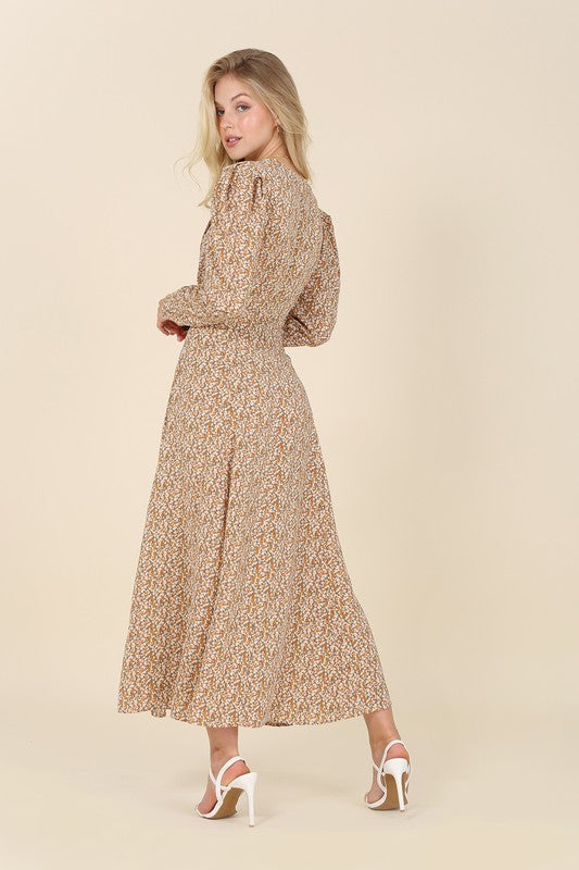 A woman gracefully poses against a beige background wearing the Fit and Flare floral maxi dress, featuring a V-neckline, elegant puff sleeves, and a complementary front slit.