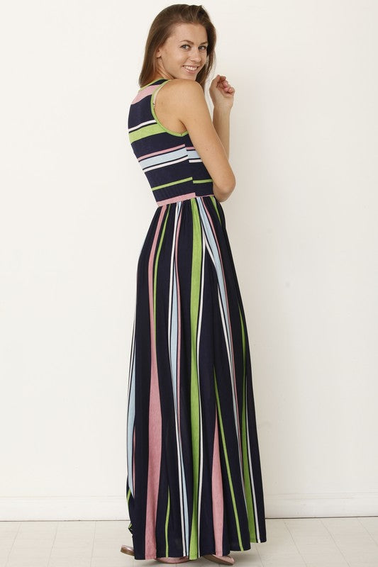 A person wearing the Multi Stripe Rainbow Maxi Dress stands against a plain background, hands in pockets and smiling.