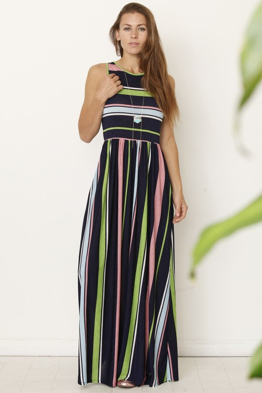 A person wearing the Multi Stripe Rainbow Maxi Dress stands against a plain background, hands in pockets and smiling.