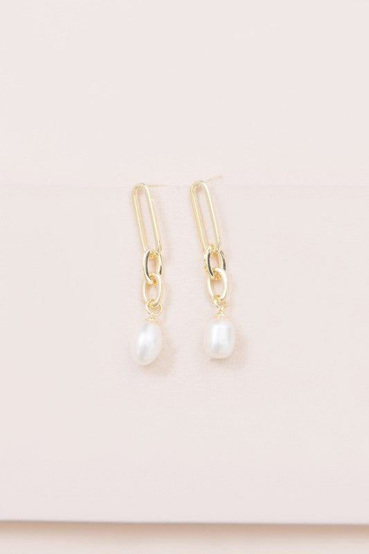 The Secured Pearl Drop Earrings showcase 14k gold plated chains with freshwater pearl pendants, artistically presented against a light background.