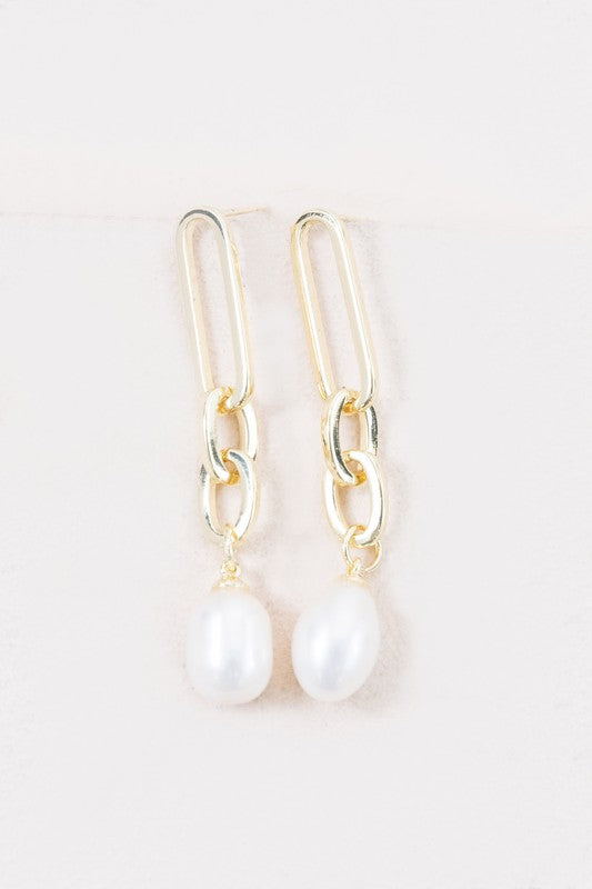 The Secured Pearl Drop Earrings showcase 14k gold plated chains with freshwater pearl pendants, artistically presented against a light background.