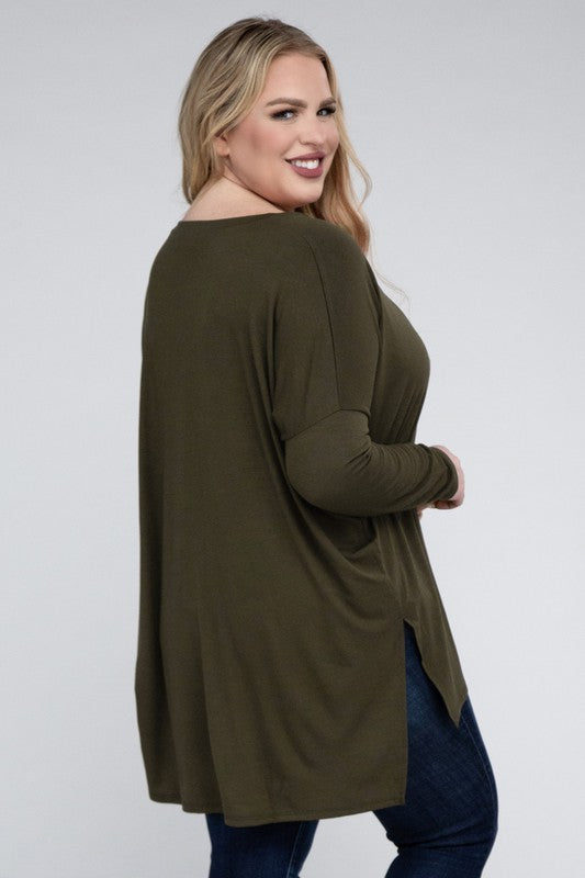 A woman with long, blonde hair wears a Plus Dolman Sleeve V-Neck Side Slit Hi-Low Hem Top and blue jeans, posing with one hand on her hip and smiling at the camera.