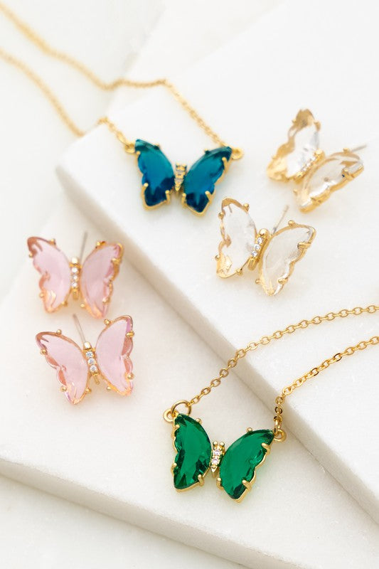 The Gem Stone Butterfly Pendant Necklace, available in an assortment of pastel hues and adorned with exquisite gemstone accents, is featured alongside matching earrings in shades of green, blue, pink, and clear, all elegantly displayed on a white surface.