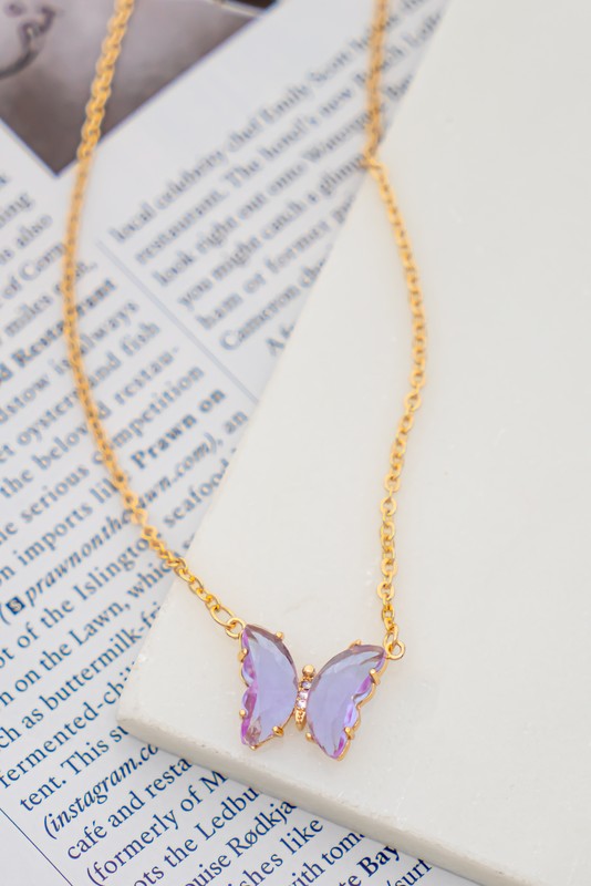 The Gem Stone Butterfly Pendant Necklace, available in an assortment of pastel hues and adorned with exquisite gemstone accents, is featured alongside matching earrings in shades of green, blue, pink, and clear, all elegantly displayed on a white surface.