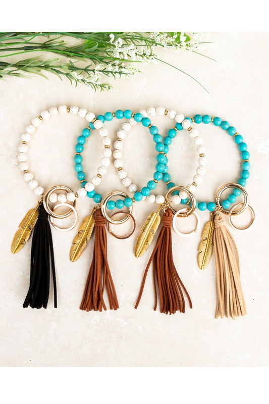A Boho Stone Key Ring Bracelet with a suede tassel and charm keychain on a person's wrist, with a car key attached.