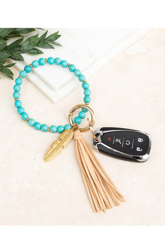 A Boho Stone Key Ring Bracelet with a suede tassel and charm keychain on a person's wrist, with a car key attached.