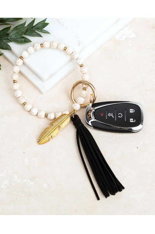 A Boho Stone Key Ring Bracelet with a suede tassel and charm keychain on a person's wrist, with a car key attached.